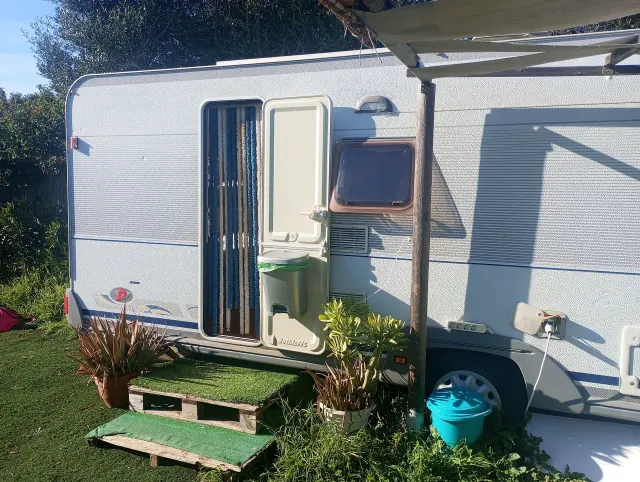 BookNoFees : location de vacances à El Palmar De Vejer – Extérieur d'une caravane ancienne avec la porte ouverte, un auvent et des plantes en pot sur l'herbe