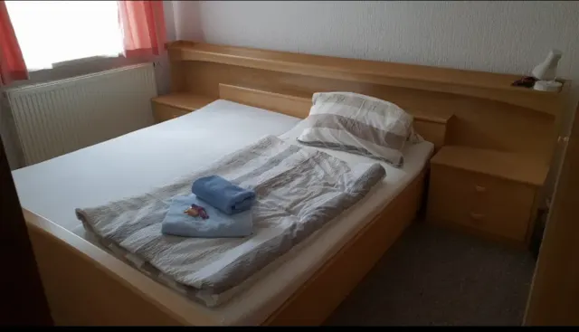 BookNoFees : location de vacances à Schönfeld – Chambre à coucher avec un lit en bois, des serviettes pliées et une fenêtre ornée de rideaux roses