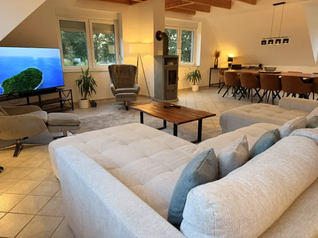 BookNoFees : location de vacances à Stuhr – Salon avec canapé en L, poêle à bois et coin repas avec table en bois