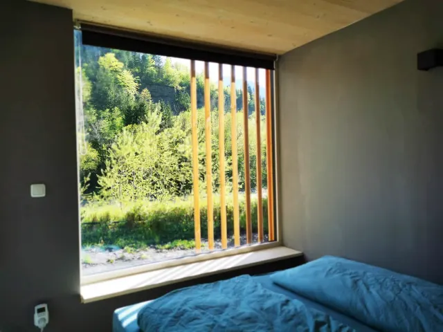 BookNoFees : location de vacances à Hieflau, Styrie, Autriche – Chambre à coucher avec une parure de lit bleue et une grande fenêtre à persiennes en bois donnant sur la forêt