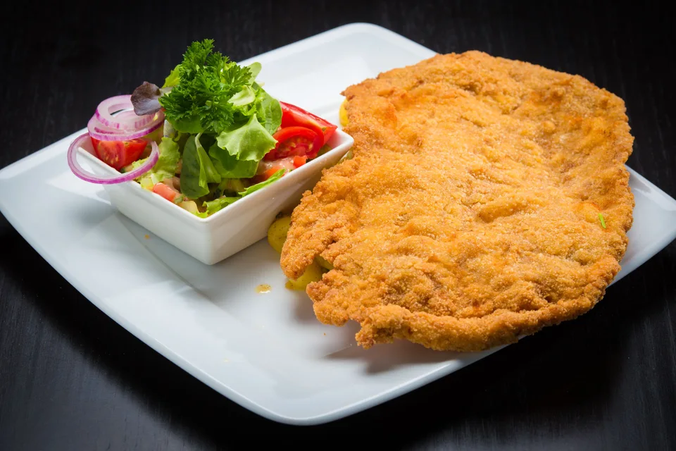 BookNoFees: Photo d’illustration : Schnitzel pané accompagné d'une salade, présenté sur une assiette blanche